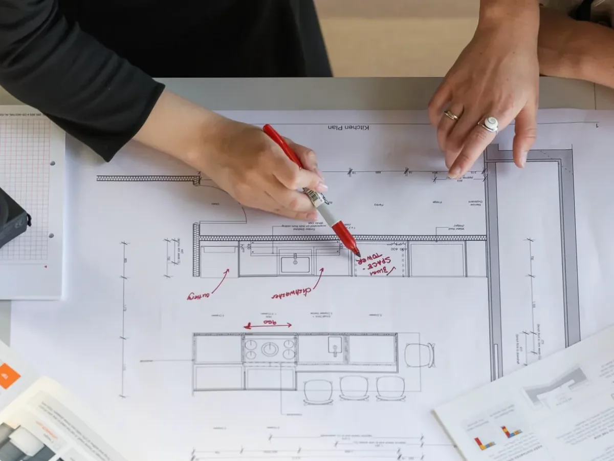 Hands marking a kitchen layout plan with a red pen