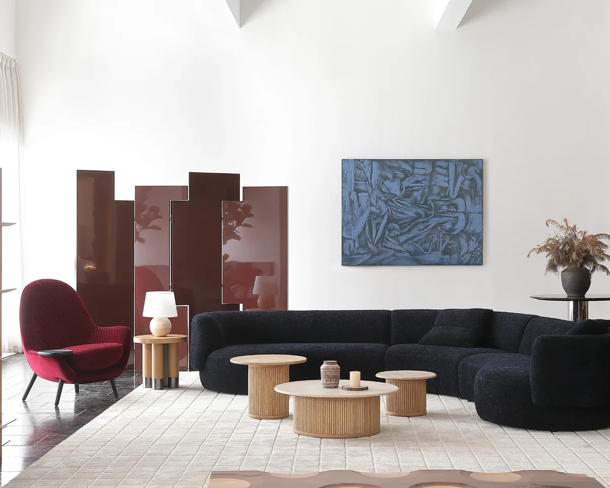 Living room with a curved black sectional, a red lounge chair and a set of round timber coffee tables