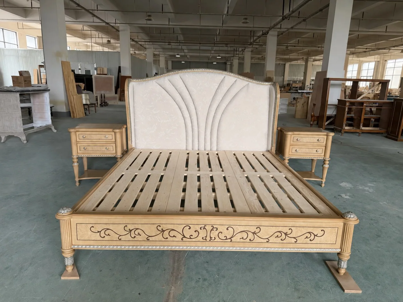 Factory floor photo of a cream upholstered solid wood bed frame with matching nightstands