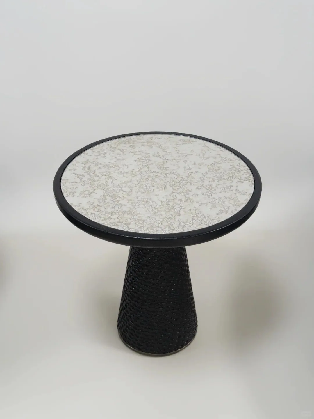 A sculptural black side table with a textured pedestal base and stone-look top.