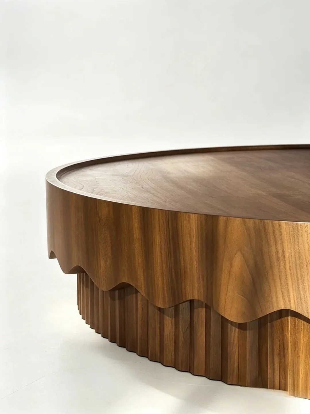 Close-up detail of a low round coffee table with scalloped edge and fluted base.