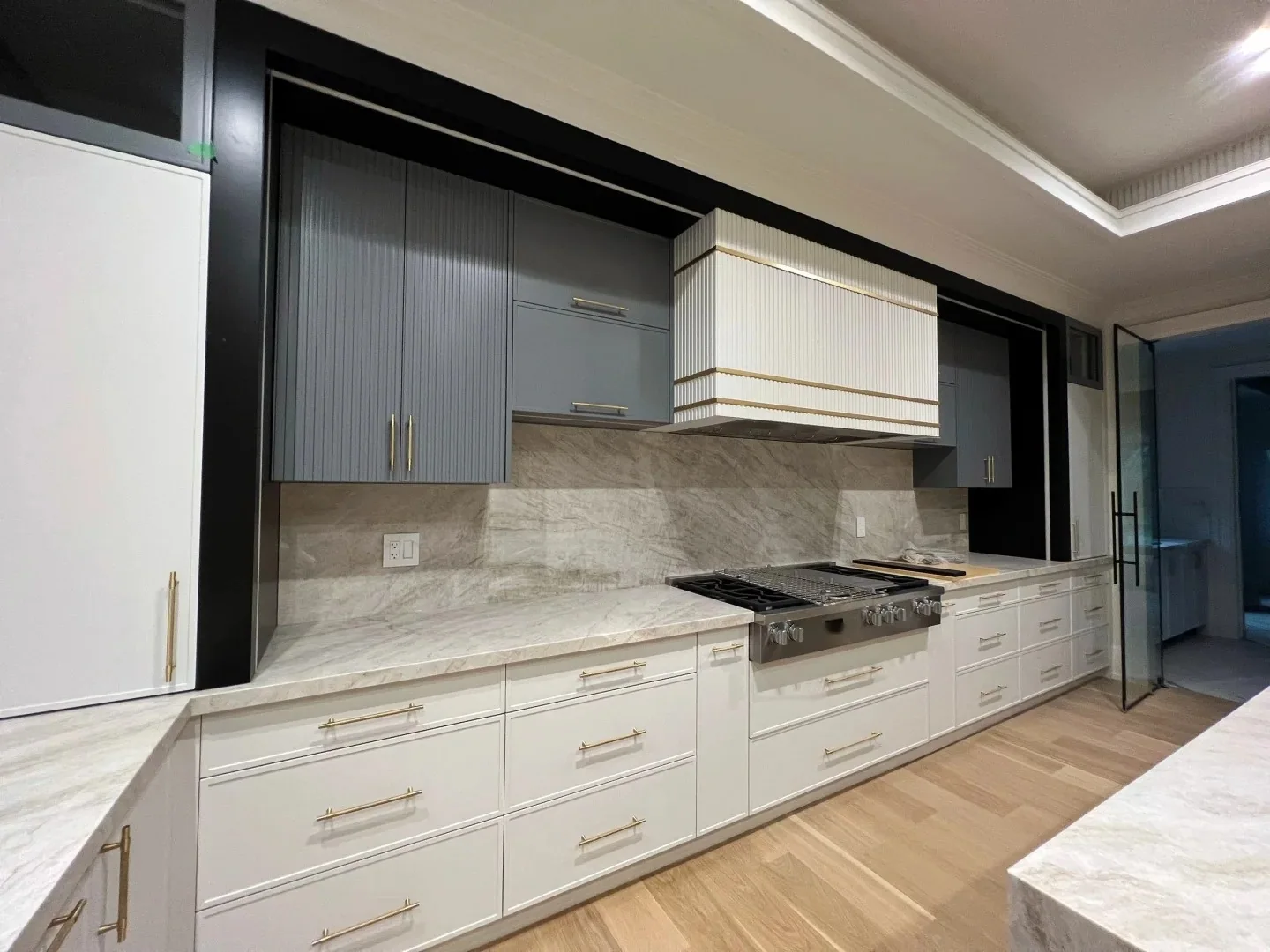 Two-tone custom kitchen cabinetry with dark upper cabinets, white base cabinets, stone surfaces and brass hardware