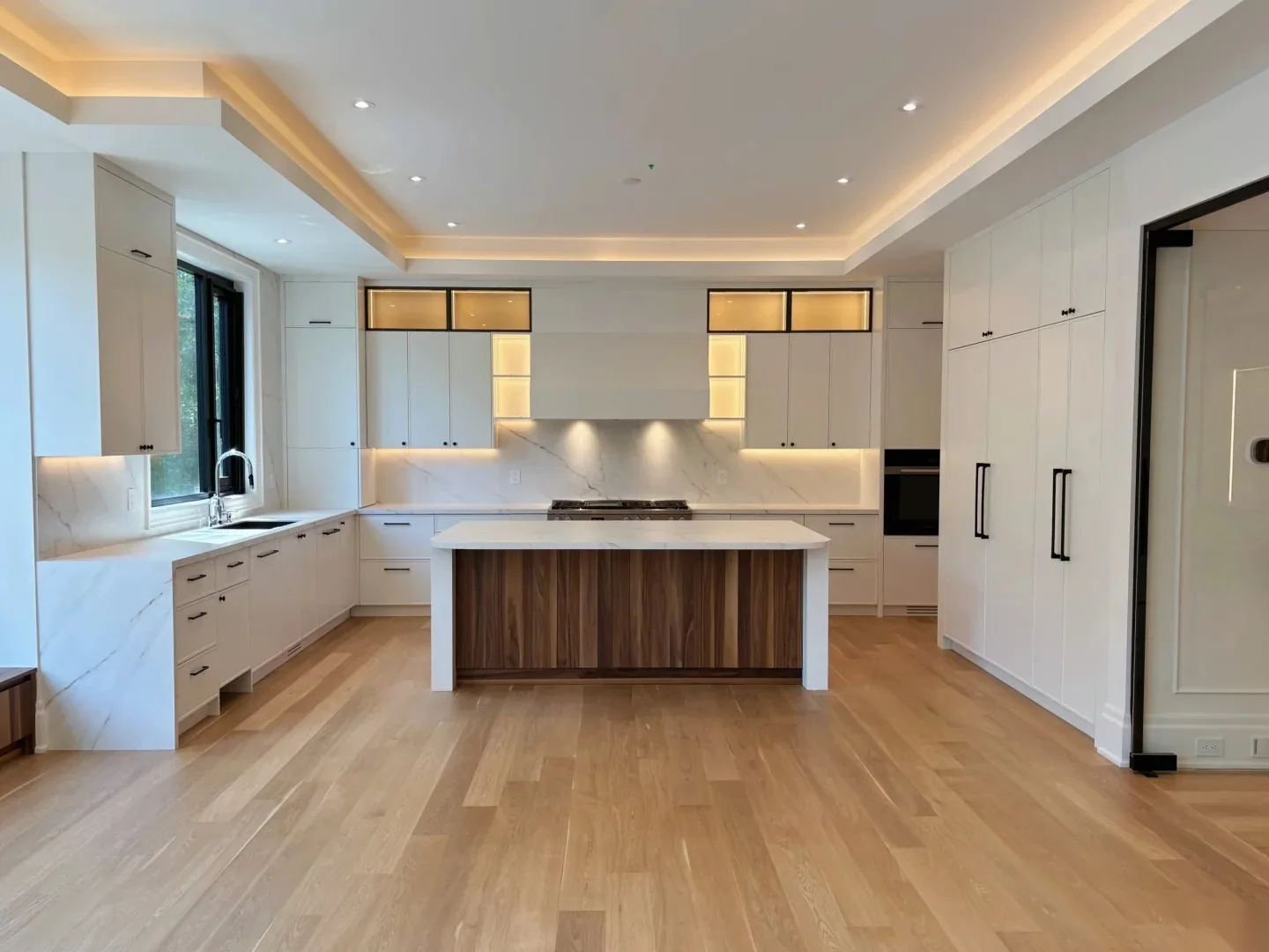 Whole-room custom kitchen with island, tall storage, integrated lighting and coordinated wall cabinetry