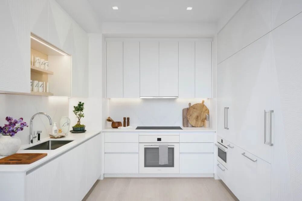 Minimal white apartment kitchen with integrated cabinetry, clean counters, and warm wood styling accents