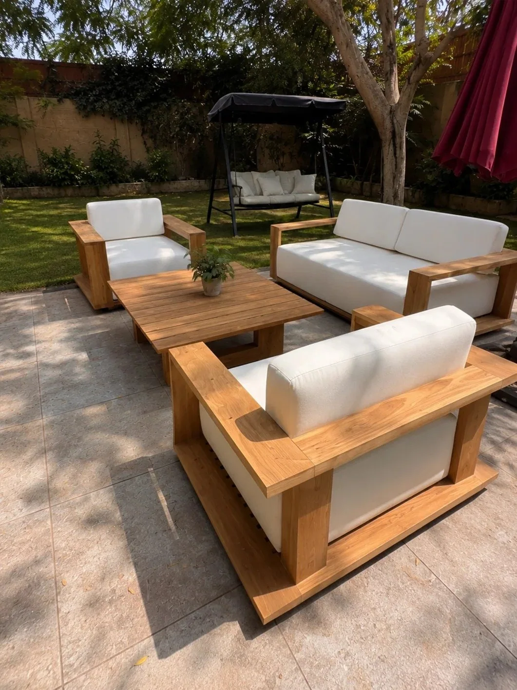 Teak outdoor sofa set with light cushions arranged on a garden patio