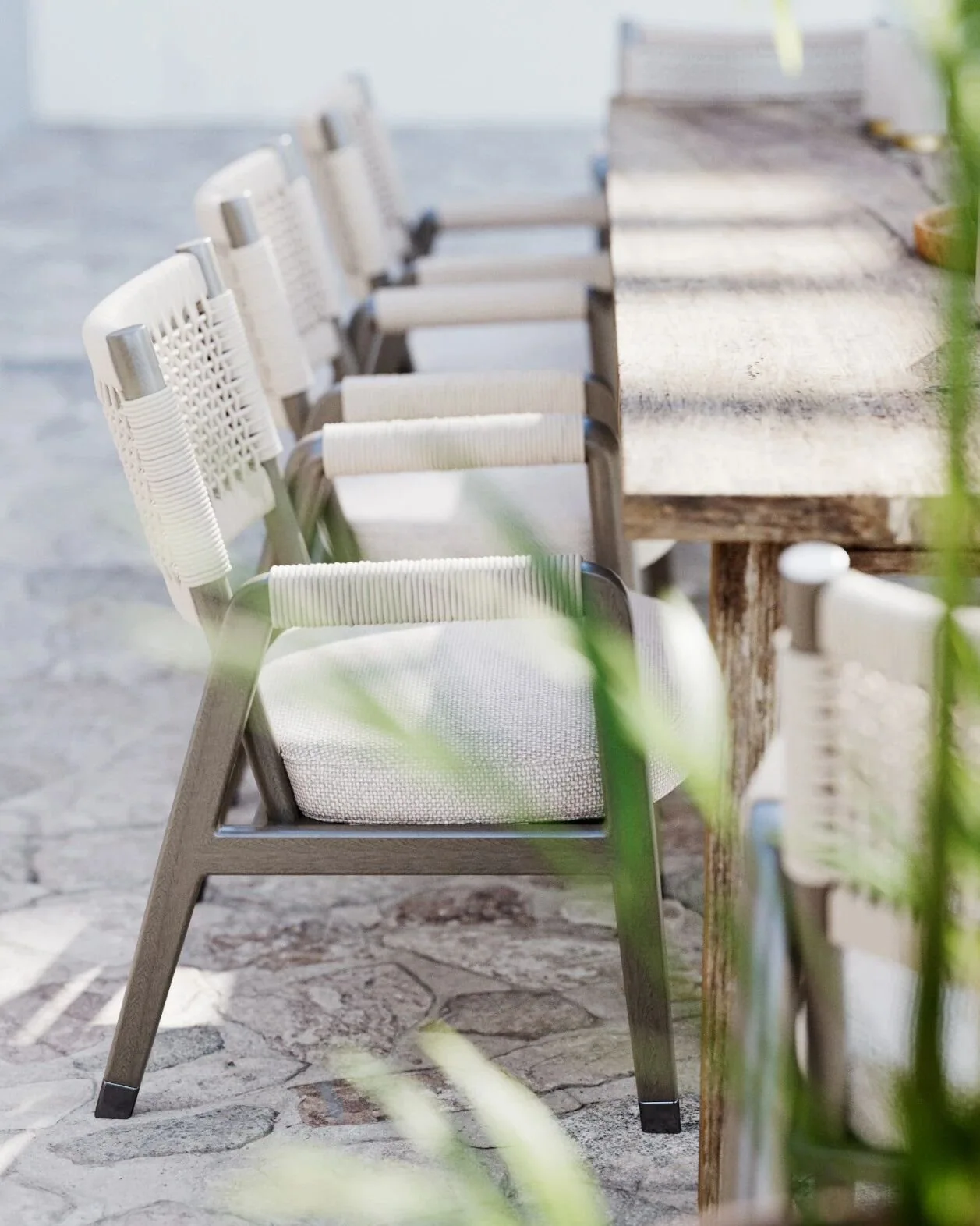 Row of rope-woven outdoor dining chairs beside a weathered wood table