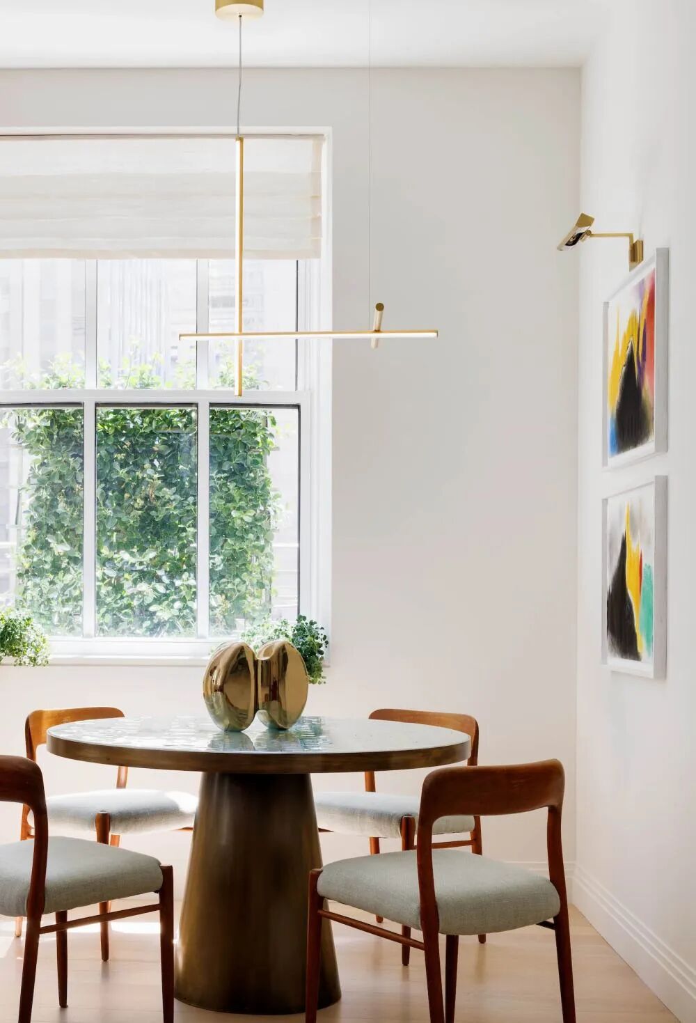 Round breakfast nook with modern pendant light, warm wood chairs, abstract wall art, and natural window light