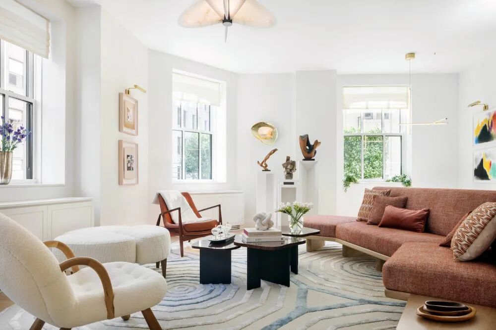 Soft modern living room with rust sofa, cream lounge chairs, sculptural coffee tables, and bright natural light
