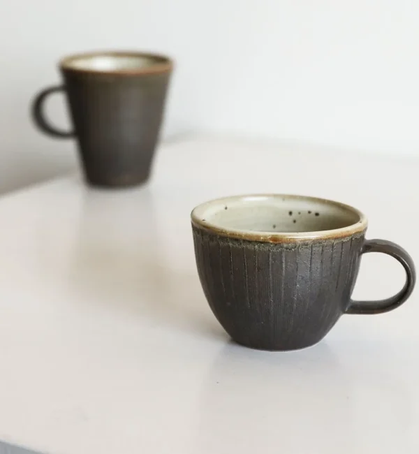 Artist Collaboration Black Glaze Ribbed Stoneware Mugs in black — in a room setting