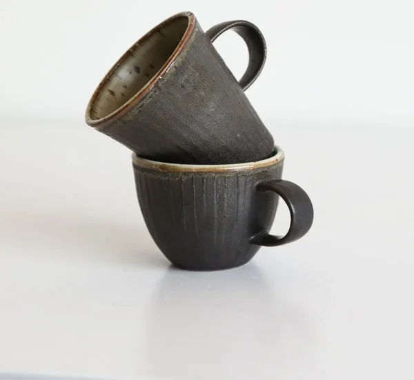 Artist Collaboration Black Glaze Ribbed Stoneware Mugs in black — in a room setting