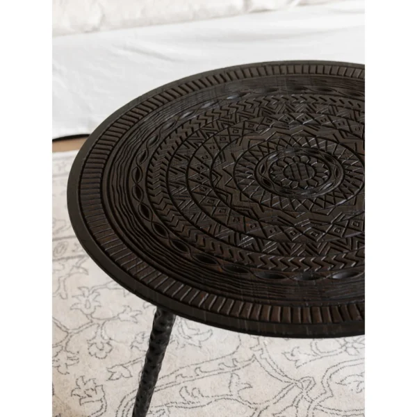 Hand-Carved Teak Round Coffee Table on Textured Metal Legs in clay — in a room setting
