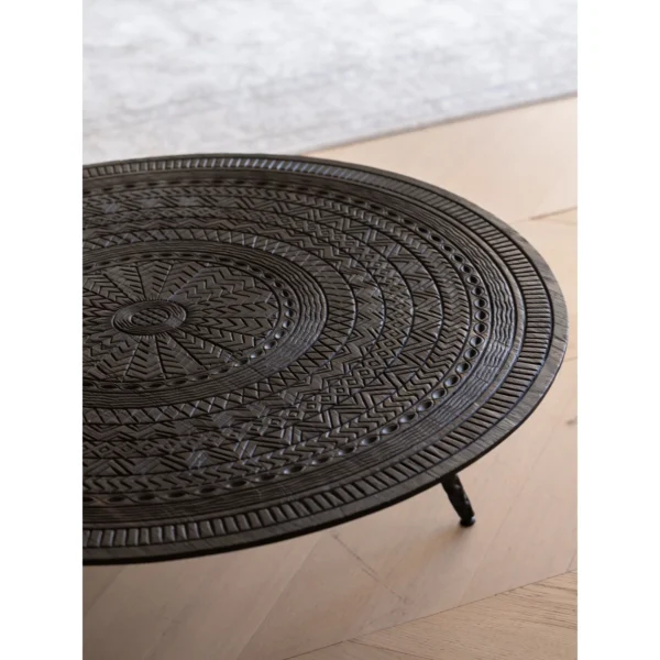 Hand-Carved Teak Round Coffee Table on Textured Metal Legs in clay — in a room setting