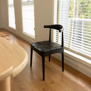 Horn-Back Teak Dining Chair with Woven Leather Seat in black — in a room setting