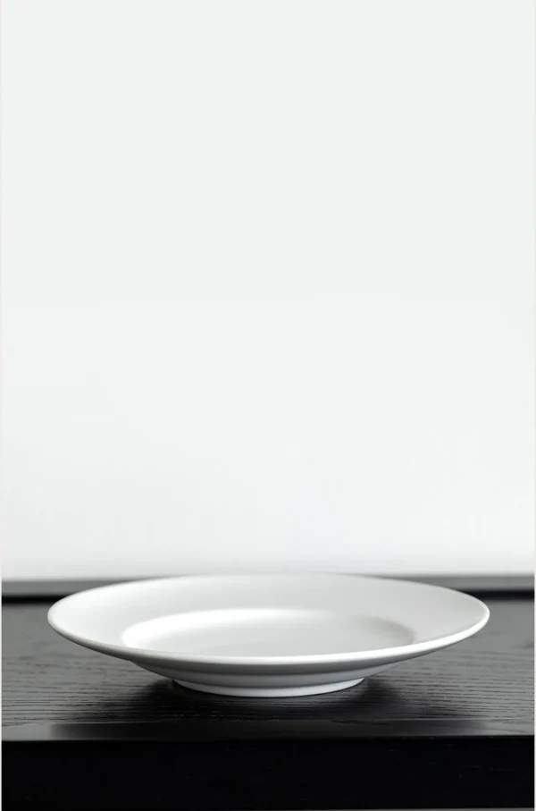 Artist Collaboration Plain Wide-Rim White Flat Plates in ivory — in a room setting