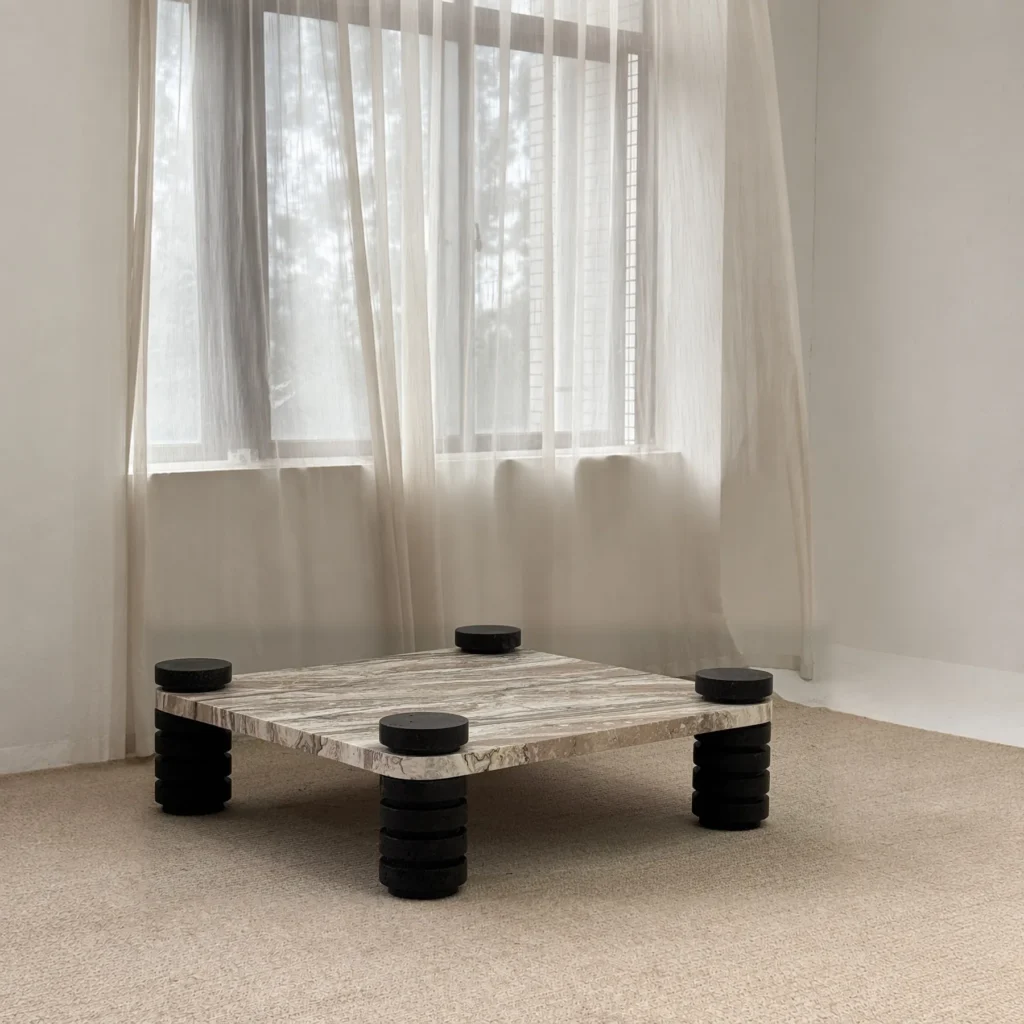 Square Travertine Coffee Table on Stacked Black Stone Legs in sand — front view