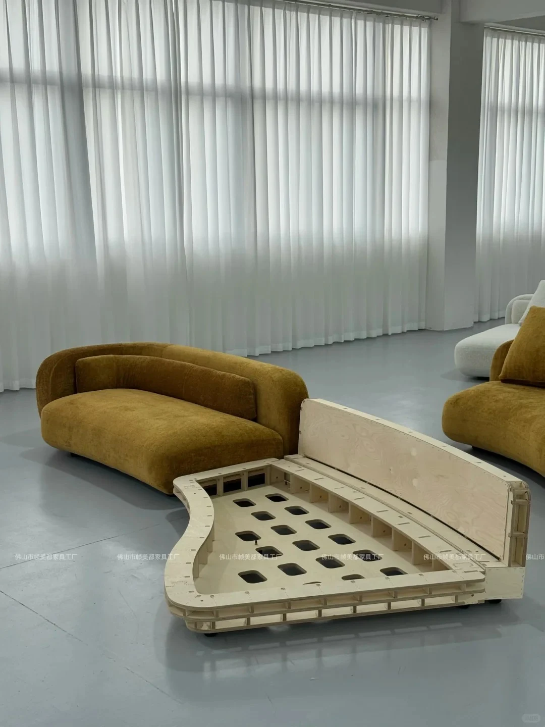 Curved sofa plywood inner frame on the factory floor next to the matching finished sofa