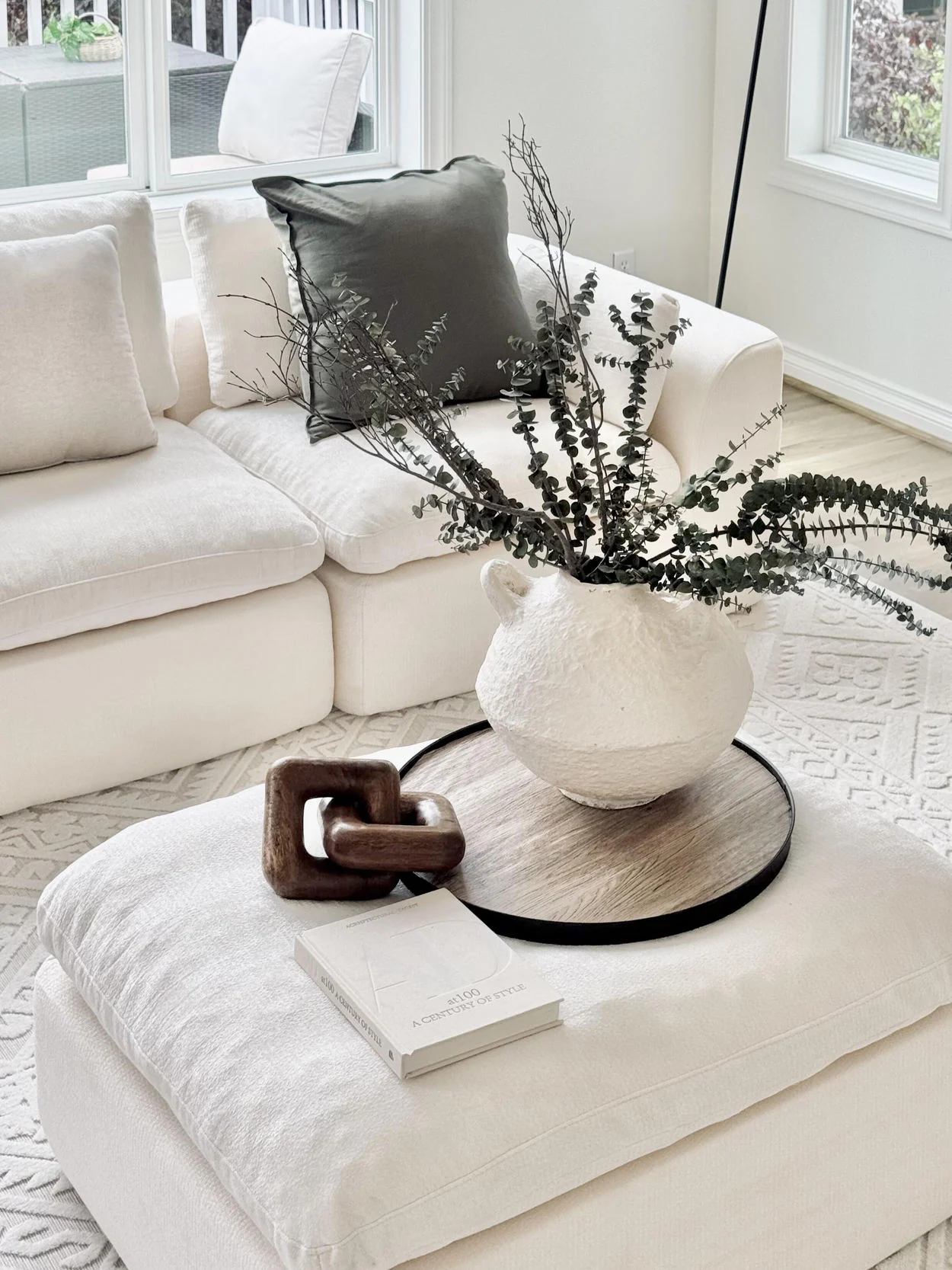 Close-up of soft cream ottoman with ceramic vase and layered textiles