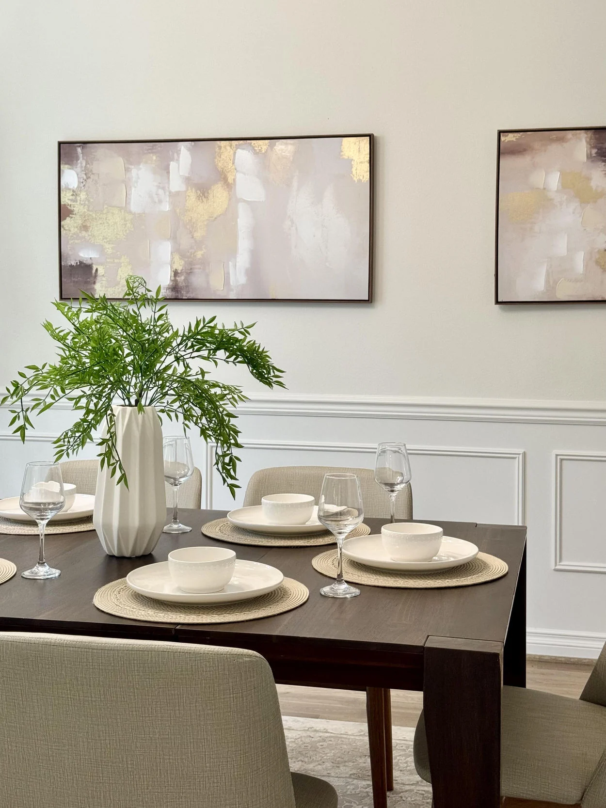 Dining table styled with simple white tableware, a plant and neutral upholstered chairs