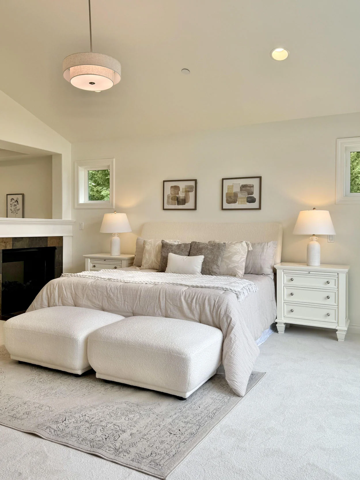 Bright bedroom with pale upholstered bed, layered ivory linens and warm bedside lamps