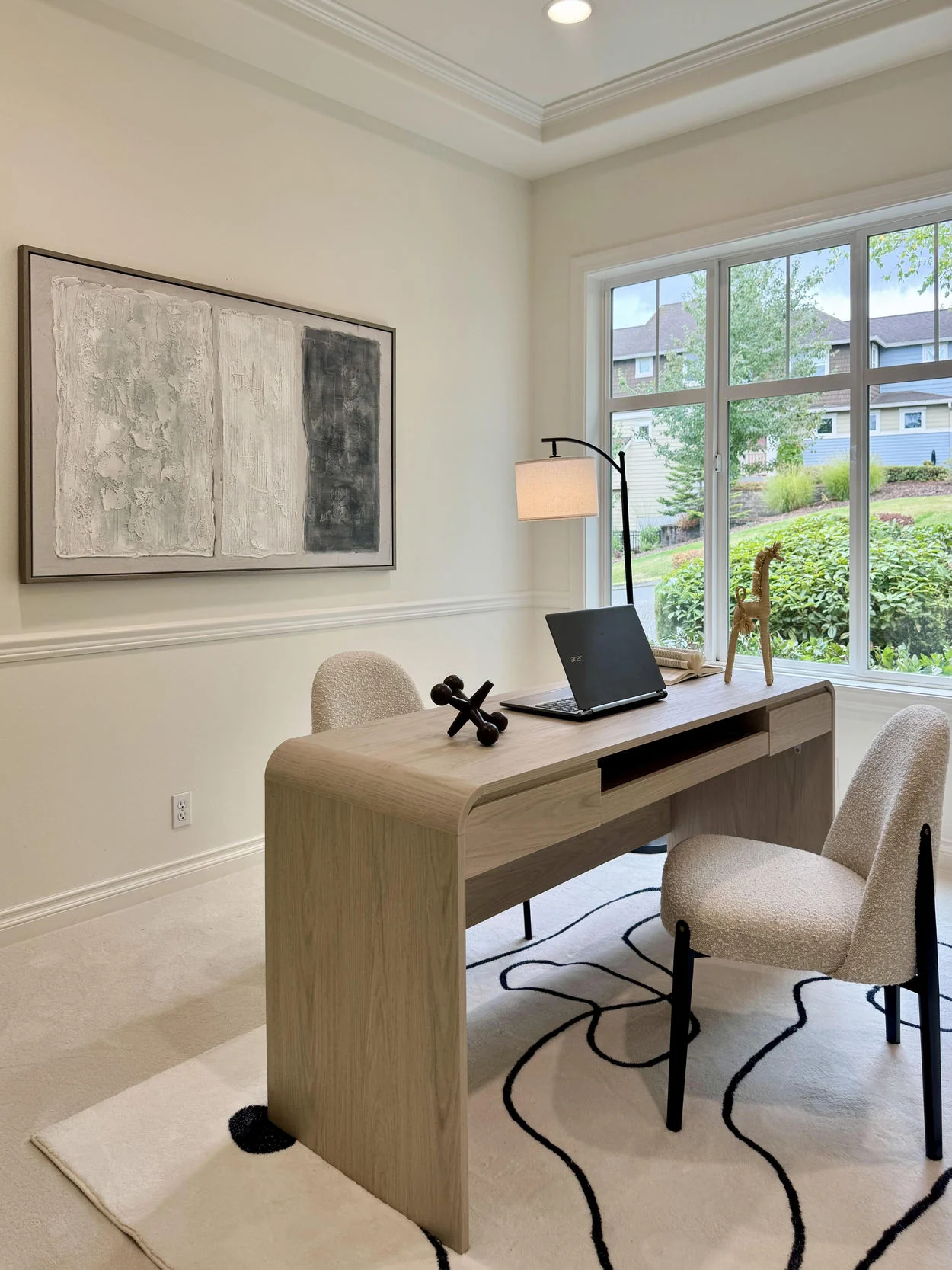 Light wood desk with upholstered chair, daylight and abstract artwork in a home office