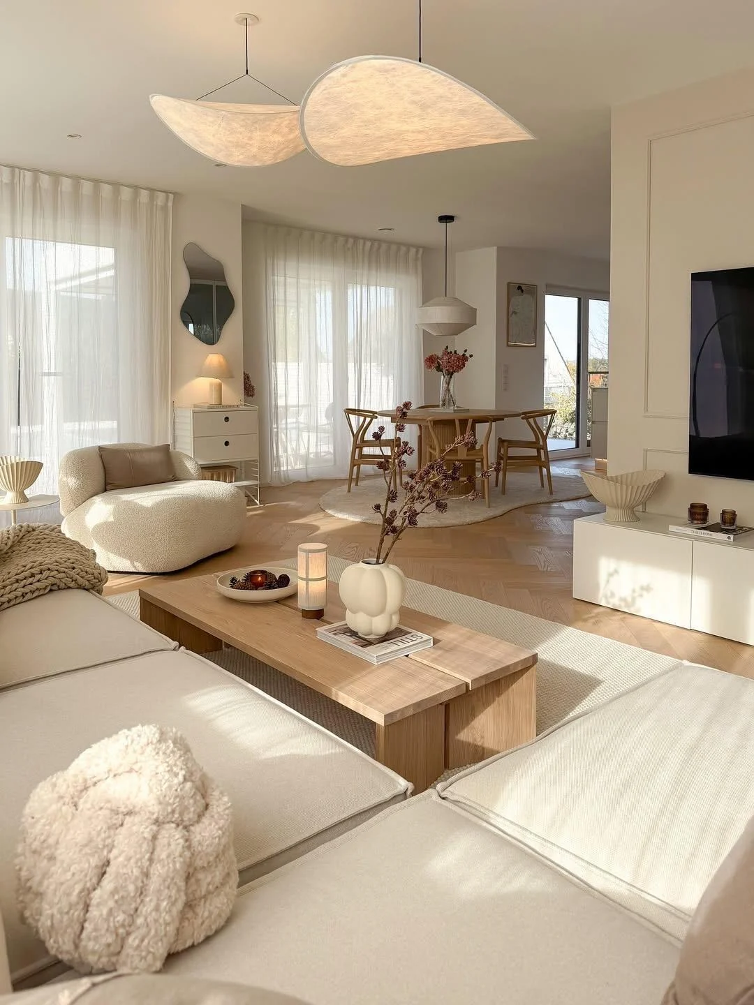 Warm Scandinavian open-plan living and dining room with natural wood furniture, creamy upholstery and sculptural pendant lights