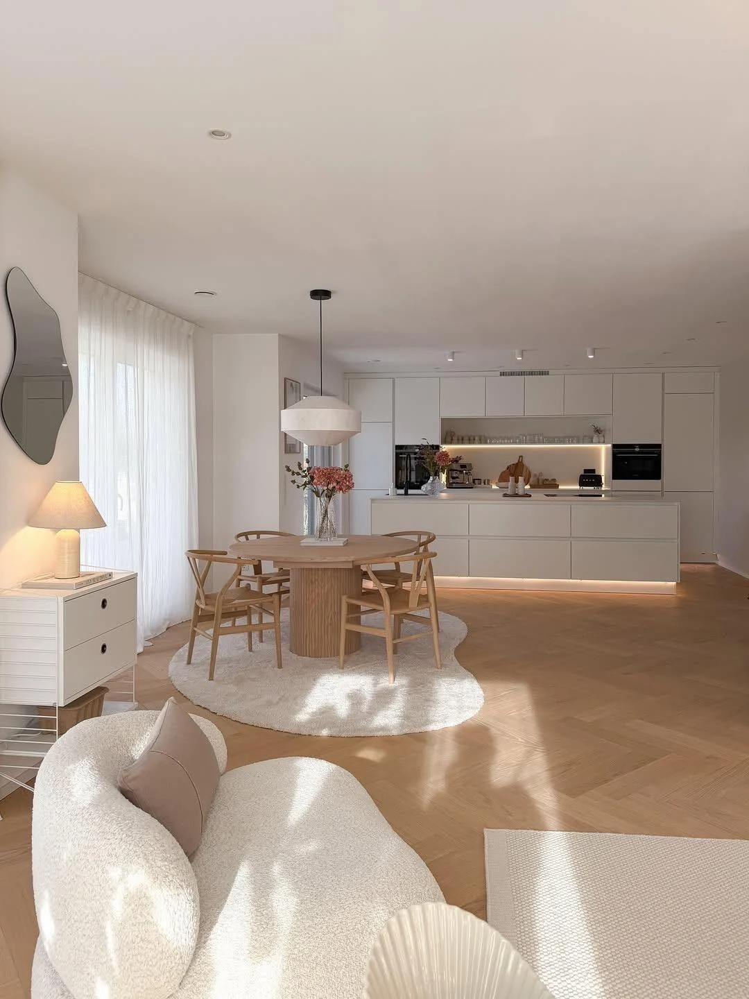 View across a Scandinavian living room toward an open kitchen and light wood dining furniture