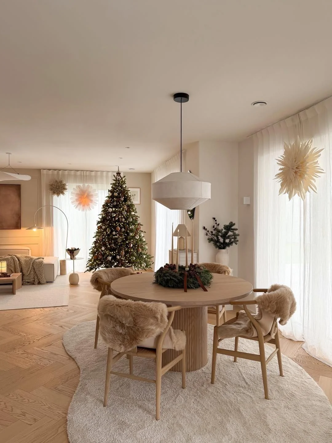 Closer view of a round Scandinavian dining table with pale timber chairs, warm light and subtle festive styling